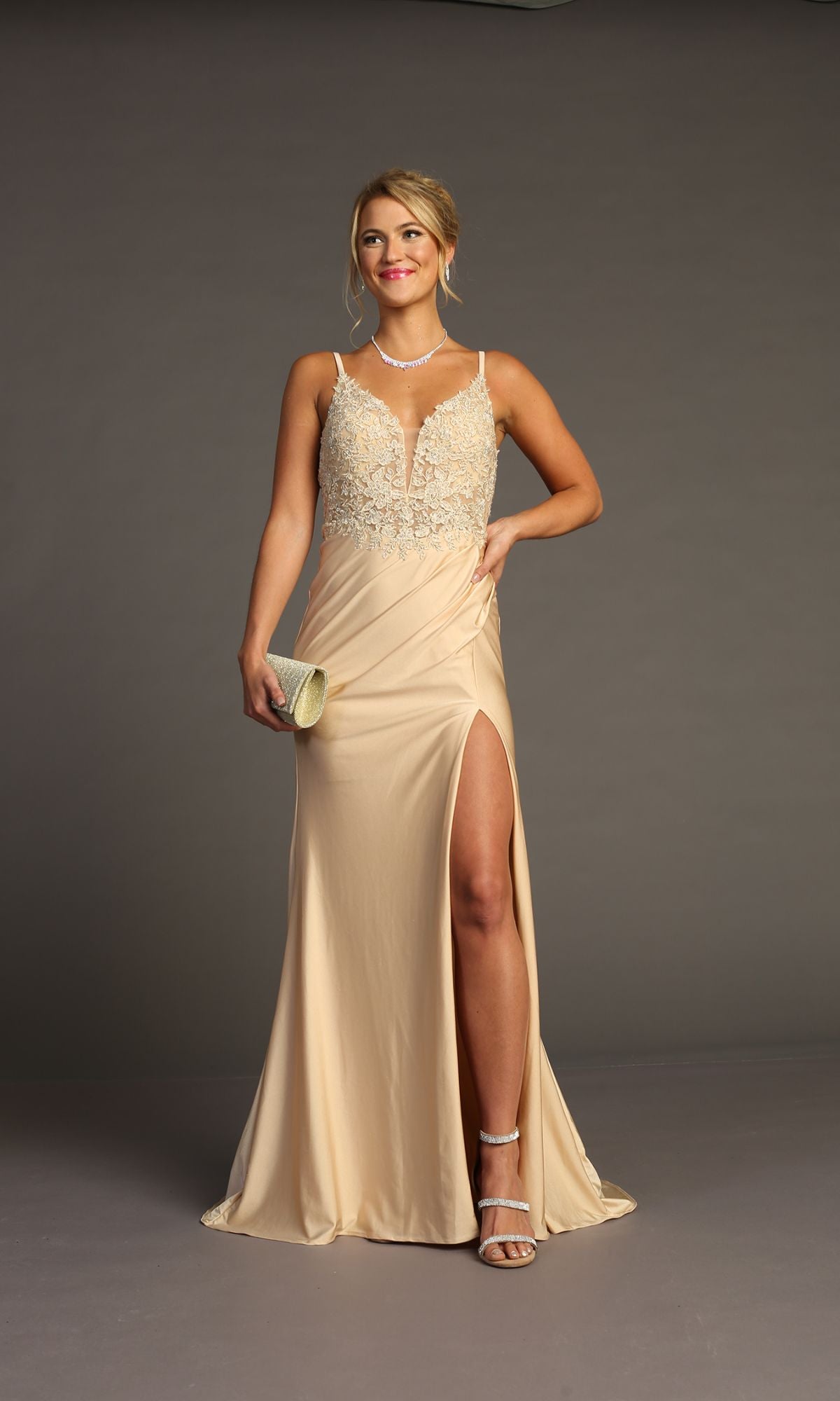 A woman in the Lace-Bodice Slinky Long Prom Dress (Chicas YG5033), a beige sleeveless evening gown with embroidered lace and a thigh-high slit, holding a clutch against a plain gray background.